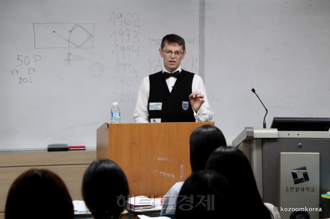 블롬달이 3쿠션 선수 경기복 차림으로 연단에 서서 학생들에게 이야기하고 있다.