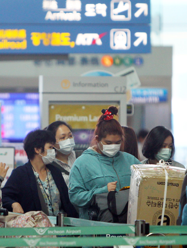 Passengers wearing masks queue to check in at Incheon International Airport in Incheon on Sunday.    Xinhua-Yonhap