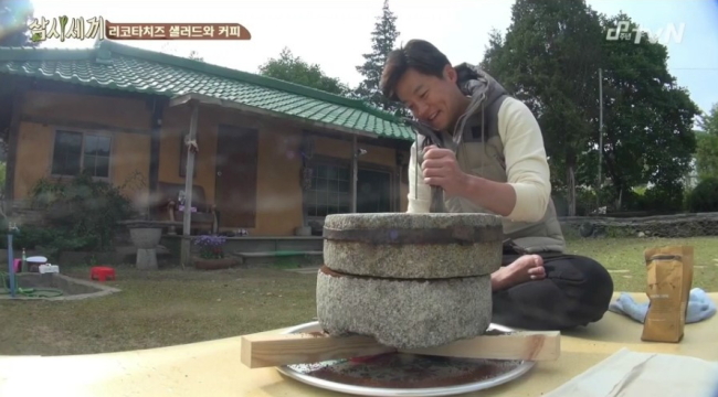 Actor Lee Seo-jin grinds coffee in a maetdol, or millstone, on cooking reality show “Three Meals a Day.”    tvN