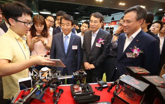Kim Chang-geun, chairman of the SK SUPEX Council (third from right, front row), Science, ICT and Future Planning 1st Vice Minister Lee Suk-joon (second from right, front row) and SK Telecom CEO Jang Dong-hyun (right, front row) examine an active Wi-Fi camera developed by THES at the Daejeon Creative Economy Innovation Center on Thursday. (SK Group)　
