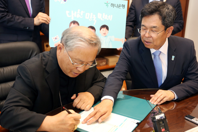 지난 6월 1일 천주교 서울대교구 교구청에서 염수정 추기경(사진 왼쪽)이 김병호 하나은행장(사진 오른쪽)의 설명을 들으며 대한민국만세 상품에 가입하고 있다. [사진=하나금융그룹]