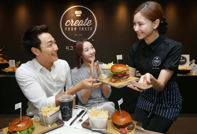 A McDonald’s Korea staff member serves the new “Signature Burger” to customers at its Sinchon store in Seoul, Wednesday.   McDonald’s Korea
