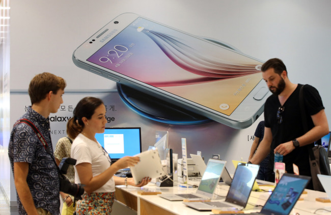 Foreign visitors look at mobile devices during their visit to a Samsung digital shop in Seoul. (Yonhap)
