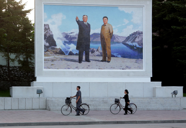 Locals push their bicycles past a large painting depicting North Korean leaders Kum Il-sung (left) and Kim Jong-il in Wonsan, North Korea, Monday. (AP-Yonhap)