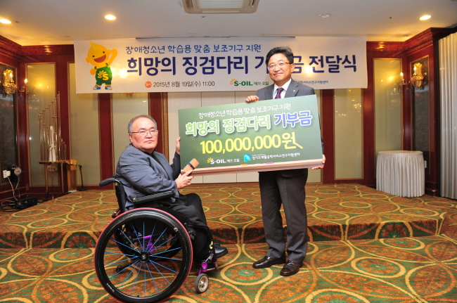 S-Oil senior vice president Lee Chang-jae (left) delivers a certificate guaranteeing 100 million won ($92,800) worth of study aids to 42 low-income disabled students at the Gyeonggi Assistive Technology Research Assistance Center in Suwon, Gyeonggi Province, last week, continuing its efforts to help disabled youths since 2010. (S-Oil)