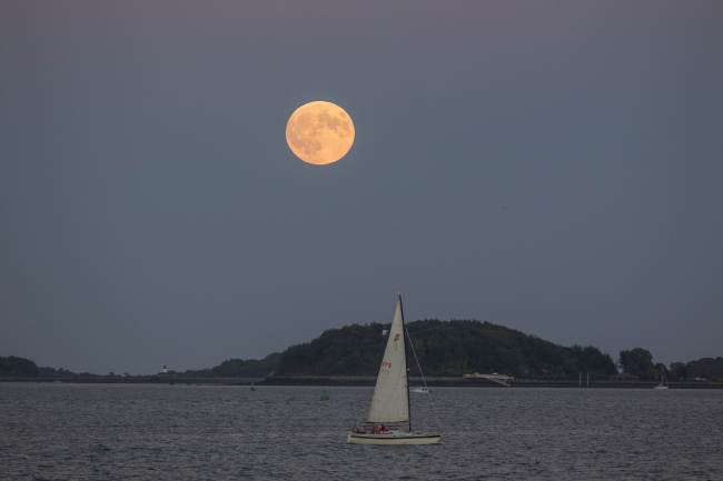 The Super Blood Moon rises over a sailboat in Boston Harbor on Sunday in Boston, Massachusetts. (Yonhap-AFP)