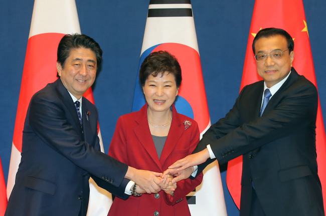 South Korean President Park Geun-hye, Japanese Prime Minister Shinzo Abe (left)and Chinese Premier Li Keqiang hold hands together for a photo before their trilateral summit at Cheong Wa Dae on Sunday. (Yonhap)