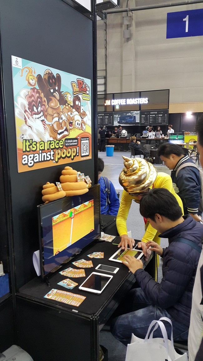 Aki Koseki (in yellow), president of Japanese indie game developer Dice Creative, explains how to play the firm’s game to a visitor at the G-Star game expo in Busan on Friday. (Kim Young-won/ The Korea Herald)