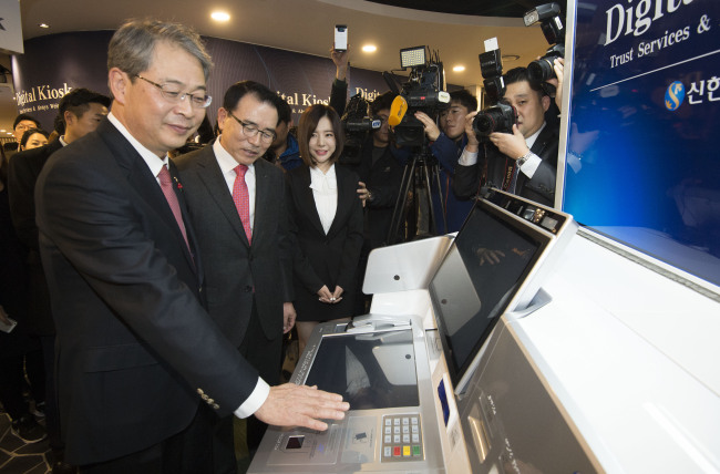 Financial Services Commission Chairman Yim Jong-yong (left), Shinhan Bank president Cho Yong-byeong (second from left) give a demonstration of venous authentication at a digital kiosk in the bank‘s main office in Seoul on Wednesday.   Yonhap