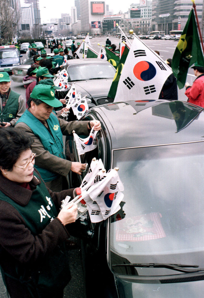 Volunteers give out Taegeukgi in downtown Seoul during the government’s campaign to promote the hoisting of the national flag ahead of the March 1 Independence Movement Day early this year.   The Korea Herald