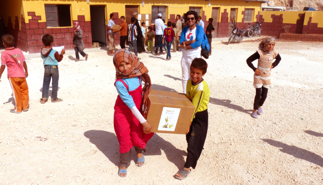 Syrian children carry aid boxes provided by the Help Syria humanitarian organization last year. In the blue shirt is group director Abdul Wahab Almohammad Agha.   Help Syria