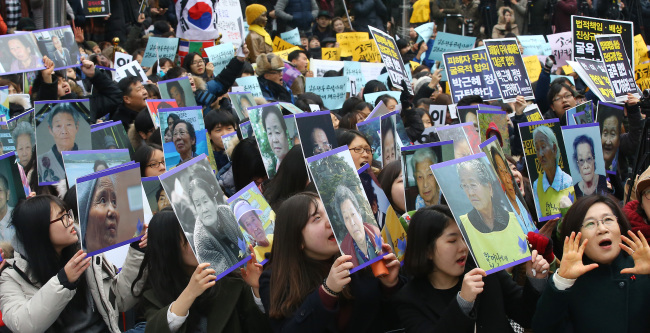 Participants hold up pictures of victims of Japan's WWII sexual slavery during a weekly rally held near the statue of a girl representing comfort women adjacent to a construction site of the Japanese Embassy building in central Seoul, Wednesday. (Yonhap)