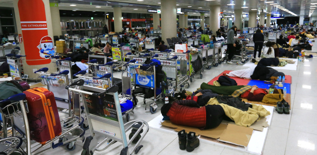 Passengers rest on the floor at Jeju International Airport‘s passenger terminal early Monday.  Yonhap