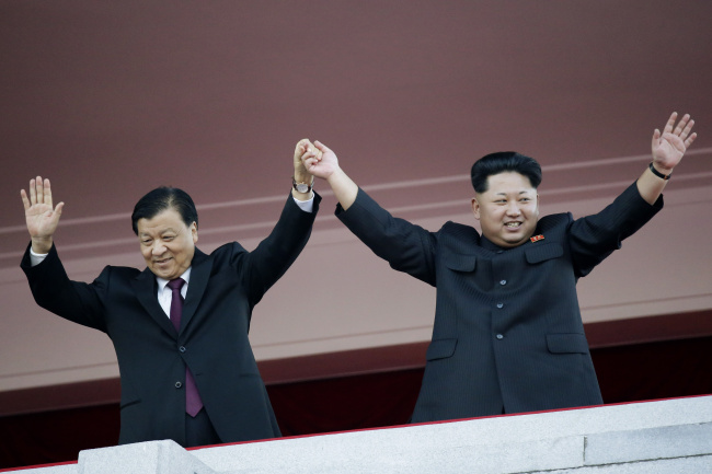 Liu Yunshan (left), a member of the Standing Committee of the Chinese Communist Party, and North Korean leader Kim Jong-un lift their hands together while watching a military parade to mark the 70th anniversary of North Korea’s ruling Workers’ Party last October. Yonhap