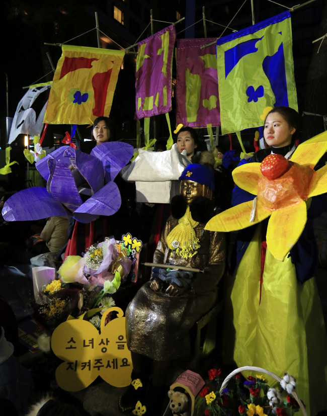 Students holding works of art stand around a “comfort women” statue opposite the Japanese Embassy in Seoul on Saturday in their fifth weekly protest against the Korea-Japan deal.  Yonhap