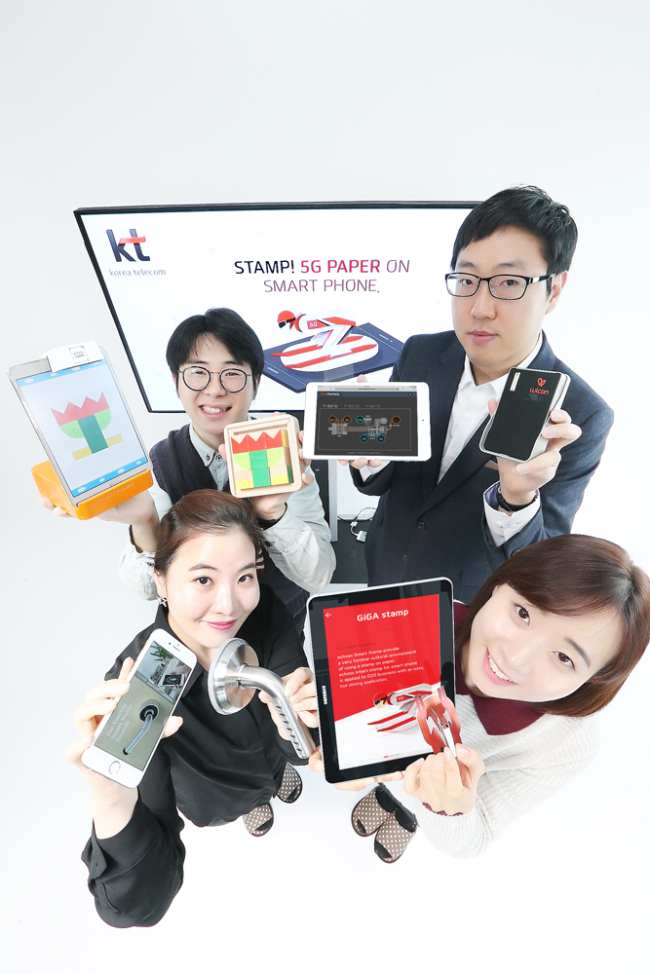 KT staffers hold products developed by start-ups. Clockwise from top left are smart toy bricks developed by Atto Cube, a smart factory solution developed by Ulalalab, 12CM’s digital stamp and Amadas’s smart door lock. (KT)