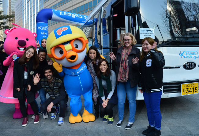 K-Travel Bus passengers pose for a photo Friday with popular Korean animation character Pororo, selected as a promotional ambassador for Korean tourism, in front of K-Travel Bus buses. (Yoon Byung-chan/The Korea Herald)
