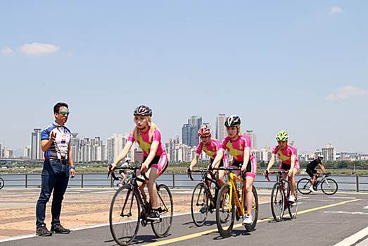 Rookie girl group SOL-T members, honarary ambassadors of Ironman 70.3 Busan, train for cycling with Park Byung-hoon (left), the vice president of  Korea Triathlon Union. (Emerson K Partners)