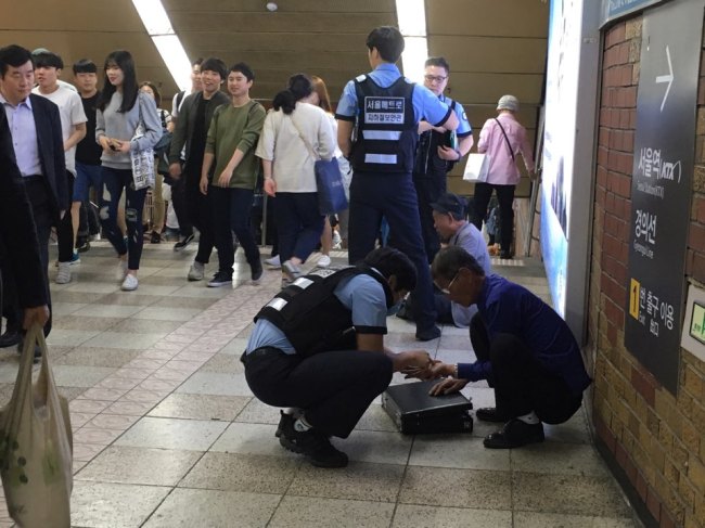 Subway Guards talk to a homeless person sitting in a station near a subway track on Line No. 4 in Seoul Station on Wednesday. (Jo He-rim/The Korea Herald)