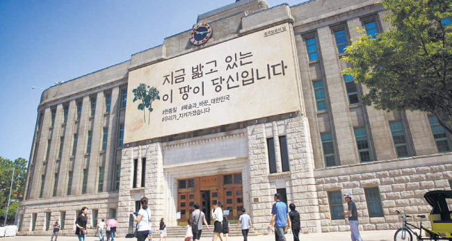 서울광장 앞 서울도서관 외벽‘ 꿈새김판’에‘ 지금 밟고 있는 이 땅이 당신입니다’ 글귀 앞을 지난 6일 현충일에 시민들이 지나가고 있다. 서울시는 6월 호국보훈의 달을 맞아 6일 이땅을 지키기 위해 산화한 호국영령들의 고귀한 정신을 추모하기 위해 이 글귀를 걸었다. [사진제공=서울시]