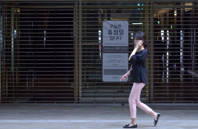 A woman walks by the close shutters of Lotte Department Store in Seoul on Monday. The Investor