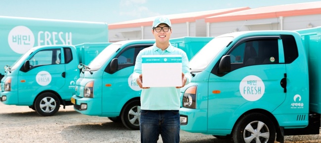 A Baemin Fresh delivery person stands in front of the company's fleet of refrigerated trucks./ The Investor