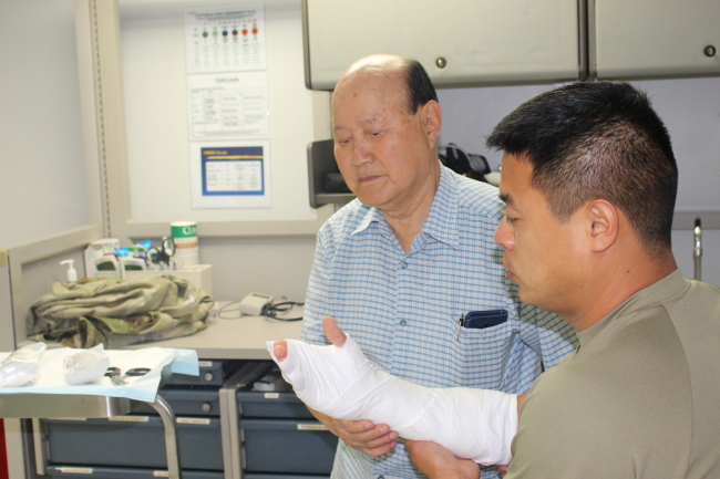 Yu Yong-bong applies bandages to a wounded U.S. soldier at the U.S. Army Garrison Daegu's Camp Walker Wood Army medical clinic, where he works as Red Cross volunteer.  (Yoon Min-sik/The Korea Herald)