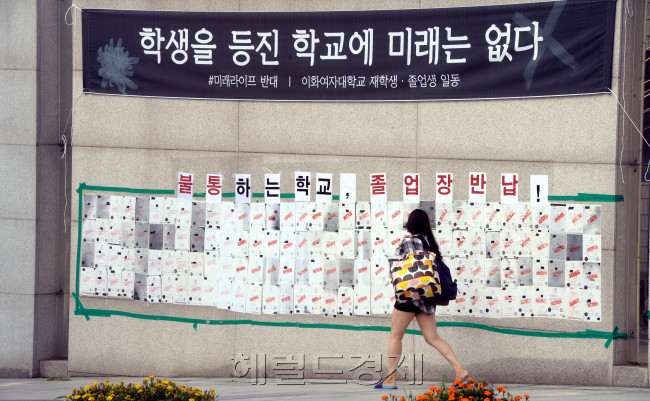 [이화여대 학생들이 학교 측의 평생교육 단과대학 사업 철회와 교육부의 수용 이후에도 총장 사퇴를 요구하며 농성을 이어갈 뜻을 밝힌 가운데 5일 오전  재학ㆍ졸업생의 본관 점거 농성이 9일째 계속되고 있다.  농성 중인 이화여대도 폭염은 비켜갈 수 없는 듯, 정문에 붙은 졸업장 반납 게시판 앞을 편한 복장을 한 여학생이 지나가고 있다.  박현구 기자/phko@heraldcorp.com]