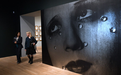 Visitors walk past a giant poster of US photographer Man Ray’s “Glass Tears” belonging to British singer-songwriter Elton John during a press preview for “The Radical Eye: Modernist Photography from The Sir Elton John Collection” at the Tate Modern in London, Tuesday. (EPA-Yonhap)
