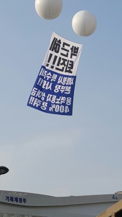 [사진설명=‘최순실 게이트’로 박근혜 대통령에 대한 국회 탄핵표결(9일)을 이틀 앞둔 7일 낮 ‘근혜노믹스’ 콘트롤타워인 정부세종청사 기획재정부 상공에 ‘박근혜 퇴진!!’ 애드벌룬이 찬바람에 휘날리고 있다. 이 애드벌룬에는 ‘세종청사 특수경비본부장 사퇴!!’, ‘용역노동자 상여금 400% 쟁취!!’도 함께 적혀 있다. (위 사진은 인터넷에 뜬 사진으로 각도상 청사 인근 아파트에서 촬영한 것으로 보임)]
