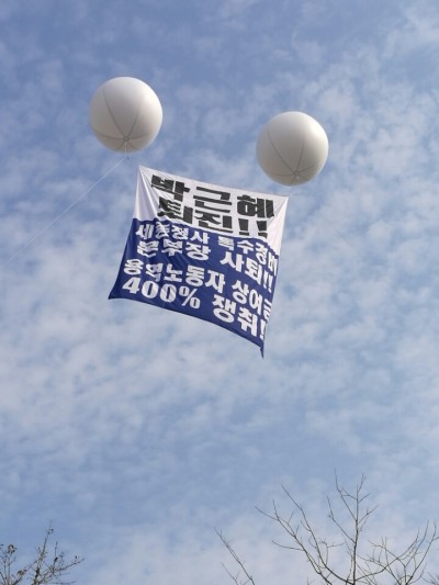 [사진설명=‘최순실 게이트’로 박근혜 대통령에 대한 국회 탄핵표결(9일)을 이틀 앞둔 7일 낮 ‘근혜노믹스’ 콘트롤타워인 정부세종청사 기획재정부 상공에 ‘박근혜 퇴진!!’ 애드벌룬이 찬바람에 휘날리고 있다. 이 애드벌룬에는 ‘세종청사 특수경비본부장 사퇴!!’, ‘용역노동자 상여금 400% 쟁취!!’도 함께 적혀 있다. (위 사진은 인터넷에 뜬 사진으로 각도상 청사 인근 아파트에서 촬영한 것으로 보임)]