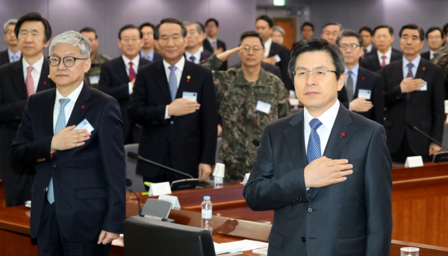 South Korea's Acting President and Prime Minister Hwang Kyo-ahn (right front) salutes the South Korean national flag during the New Year's policy briefing session on defense and diplomatic affairs at the government complex in Seoul on Wednesday (Yonhap)