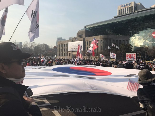 Pro-Park protestors unfurl the national flag, the icon of their rally, in Seoul Plaza on Saturday. (Bak Se-hwan/The Korea Herald)