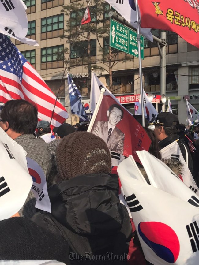 Pro-Park protestors wave the photo of Park Chung-hee, the late strongman and father of ousted President Park Geun-hye, alongside the South Korean and US national flags during a rally in Seoul Plaza on Saturday. (Bak Se-hwan/The Korea Herald)