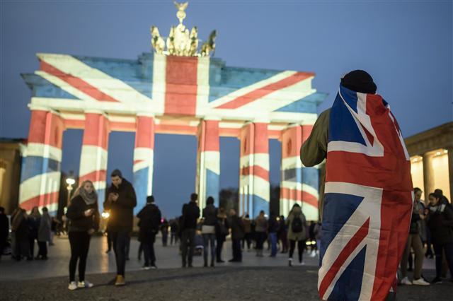 epa05866492 A man with a Union Jack on his back stands in front the Brandenburg Gate that is illuminated in the colors of the British Union Jack to show solidarity with the victims after the 22 March terror attack in central London, in Berlin, Germany, 23 March 2017. Scotland Yard in Britain said on 23 March 2017 that police have made seven arrests in raids carried out over night after the terror attack in the Westminster Palace grounds and on Westminster Bridge on 22 March 2017 leaving at least four people dead, including the attacker, and 29 people injured. EPA/CLEMENS BILAN