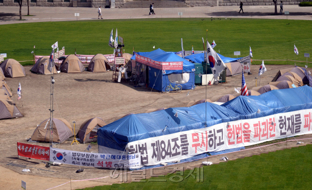 서울광장은 언제 시민의 품에 돌아오려나. 대통령탄핵과 대선을 거치며 보수단체의 메카로 등장한 서울광장 불법점유 텐트촌. '대통령 탄핵무효 국민저항 총궐기 운동본부(탄무국)' 등 보수단체가 22일 현재까지도 불법천막을 쳐놓고 서울광장을 불법점유 중이다. 대선이 끝난지 2주가 지났지만 지금도 그 후유증은 계속되고 있다. 22일 서울시에 따르면 탄무국은 1월21일 대한문에서 탄핵반대 집회를 개최하면서 서울광장에 천막 30개동을 기습적으로 설치했다. 이후 매주 토요일 대한문과 서울광장에서 대규모 인원이 참여하는 집회를 이용해 태극기·침구류·대형천막·위패를 포함해 각종 시위물품을 지속적으로 반입해 17일 기준으로 천막 41개동을 유지하고 있다. <br />24일 ‘문화가 흐르는 서울광장’공연을 준비하는 시민단체는 공연장을 서울광장 한쪽으로 옮겨 공연을 준비하고, 중앙을 차지한 텐트촌에서는 여전히 이미 재판까지 들어간 박근혜 국정농단재판에 아랑곳하지 않고 박근혜 무죄를 주장하는 방송을 계속하고 있다.<br />정희조 기자/checho@heraldcorp.com