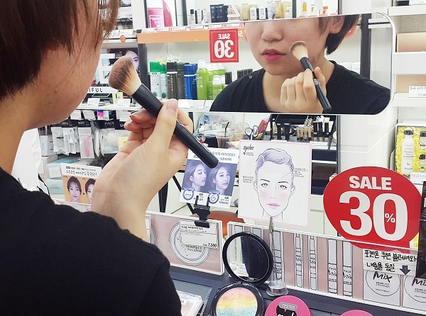 A teenager tries on makeup in a cosmetics shop in Bundang, Gyeonggi Province. (Byun Hee-jin/The Korea Herald)