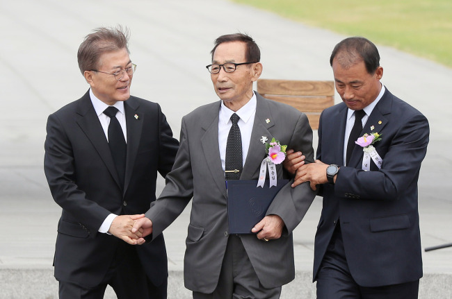 President Moon Jae-in (left) helps a meritorious person during a ceremony marking Memorial Day at the National Cemetery in Seoul on Tuesday. (Yonhap)