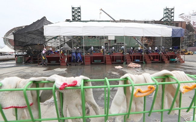 Workers sort through sand and mud from the wreckage of the sunken Sewol ferry, seen lying on its portside in the background, at Mokpo Port in South Jeolla Province on Tuesday. (Yonhap)