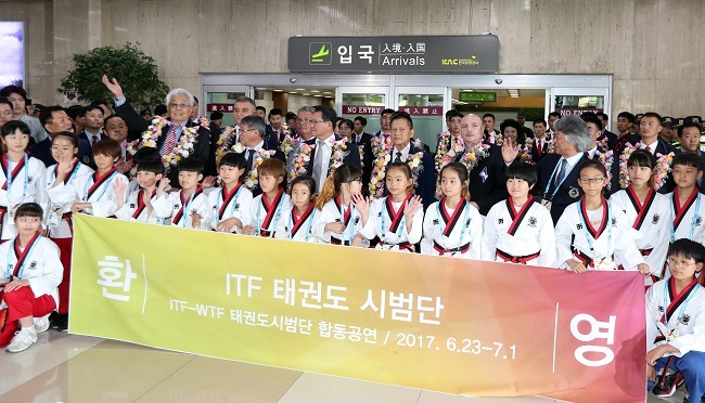 Officials and athletes of the North Korea-led International Taekwondo Federation stand behind South Korean youth taekwondo practitioners holding a welcome sign and wave to the crowd gathered at Gimpo International Airport in Seoul after their arrival on June 23, 2017. (Yonhap)