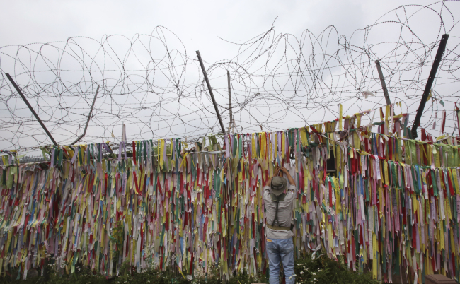 A man hangs a ribbon wishing for a reunification of the two Koreas on the wire fence at the Imjingak Pavilion, near the Demilitarized Zone of Panmunjom, in Paju, Gyeonggi Province, Sunday. (AP-Yonhap)
