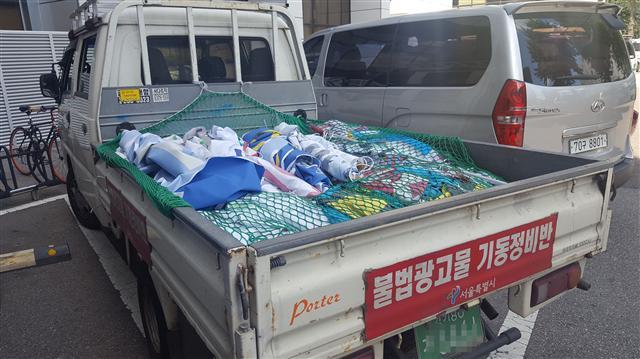 서울시 불법광고물기동정비반이 횡단보도 앞에 걸려있는 불법 현수막을 제거하고 있다. 서울시 불법광고물기동정비반이 운행하는 흰색 트럭 짐칸 모습. 하루종일 제거한 불법 현수막이 가득 쌓여있다.