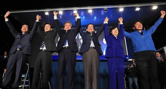 The file photo, taken May 10, 2017, shows then President-elect Moon Jae-in (third from L) holding hands with other party members to celebrate his victory in the presidential by-election held the day before. They are (from L) Goyang City Mayor Choi Sung, Seongnam City Mayor Lee Jae-myung, Moon, Seoul City Mayor Park Won-soon, Rep. Choo Mi-ae, who also heads the ruling Democratic Party, and South Chungcheong Province Gov. An Hee-jung. (Yonhap)