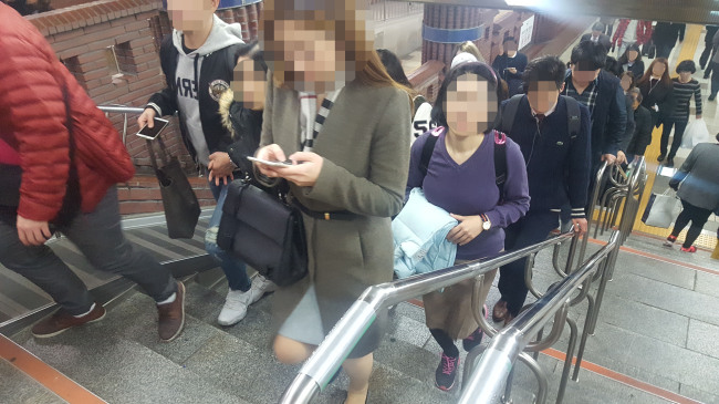 일부 시민들이 스마트폰을 보며 지하철역 내 계단을 오르고 있다.