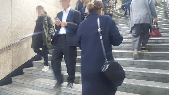 한 남성이 스마트폰에 눈길을 주며 지하철역 내 계단을 내려가고 있다.
