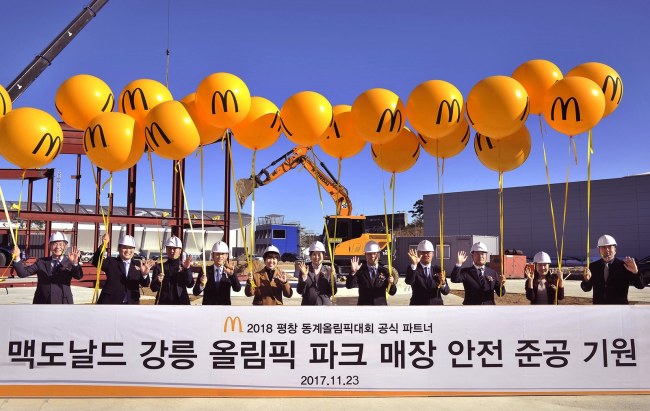 [사진=한국맥도날드 조주연 사장(가운데), 김장미 강릉 올림픽 파크 매장 점장, 매장 건축 및 운영 담당 임직원, 시공사 및 협력사 대표 등이 평창 동계올림픽의 성공적 개최와 안전한 매장 준공을 기원하며 노란 풍선을 들고 있다.]