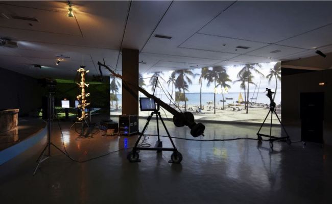 Minouk Lim, The Possibility of the Half (2012) Two-channel video projection, LED televisions, LCD monitors, prompter, SD cameras, speaker, light boxes, jimmy jib camera, burnt news desk, glass strips, sponge, wood, objects from Portable Keeper series Installation view; National Museum of Contemporary Art, Gwacheon, South Korea (Courtesy of the artist)