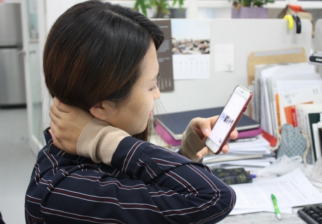 스마트폰 등의 과도한 사용으로 두통이 생겼을 때에는 스트레칭 등으로 목 주변 근육을 풀어 주는 것이 좋다. 스마트폰을 보다 두통을 느끼는 한 여성. [제공=연세바른병원]