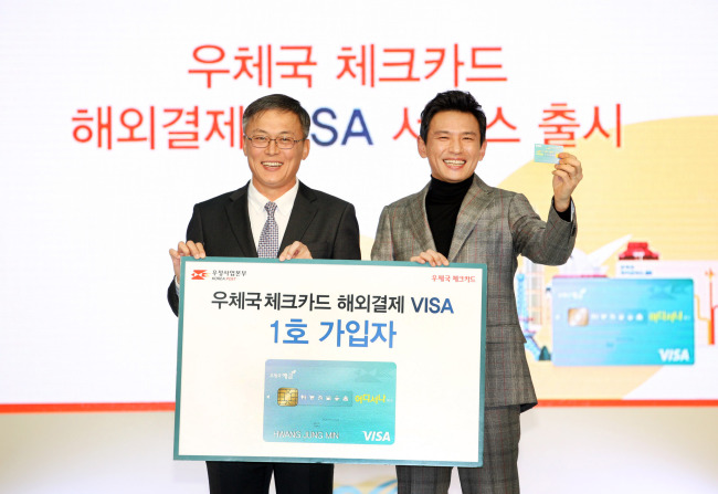 Korea Post President Kang Seong-ju (left) poses with actor and spokesman Hwang Jung-min, who became the first subscriber to the service, to mark the launch of the Visa debit card service at Incheon Airport on Tuesday. /Korea Post