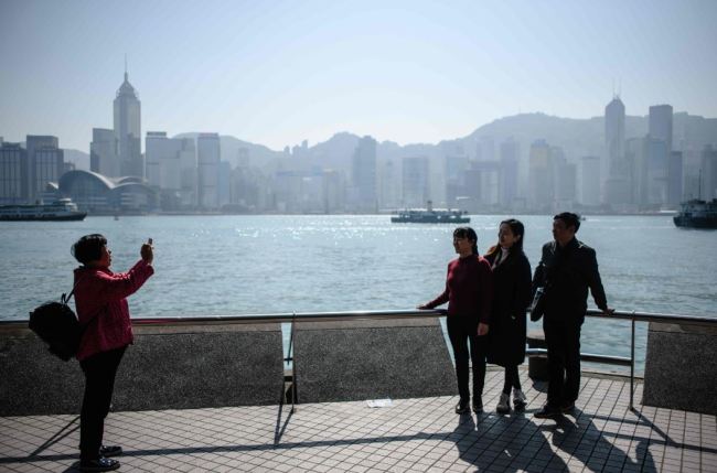 Mainland Chinese tourists pose for photos in front of Victoria Harbour and the skyline in Hong Kong on December 19, 2017. (AFP-Yonhap)